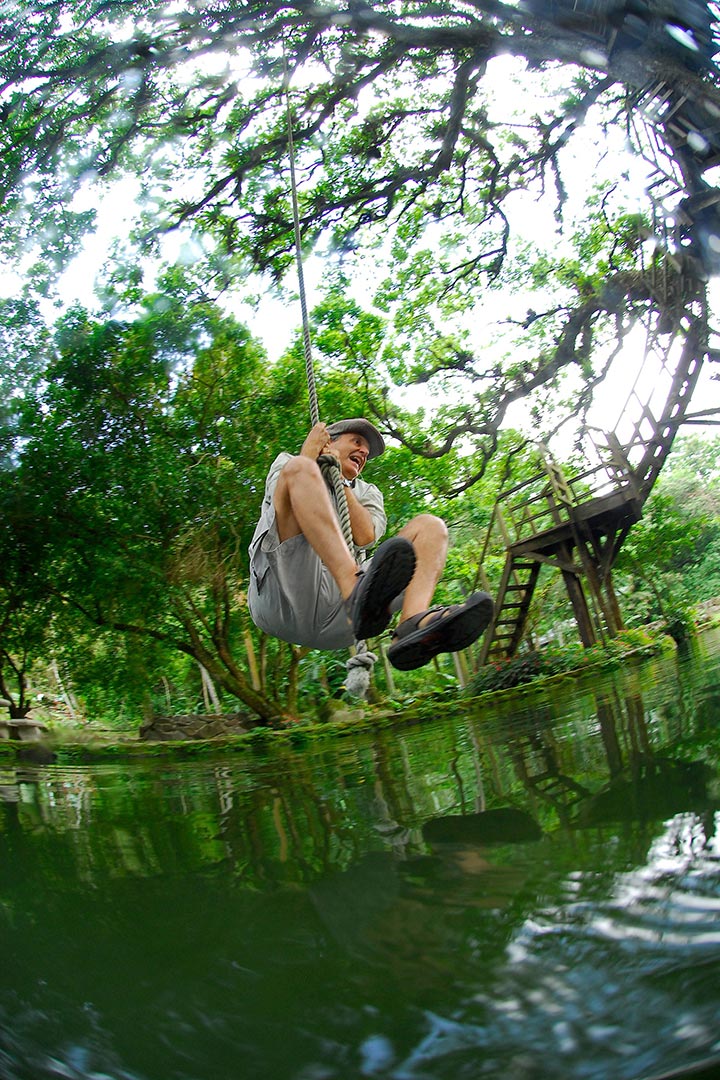 Raul swinging on rope swing over natural pool